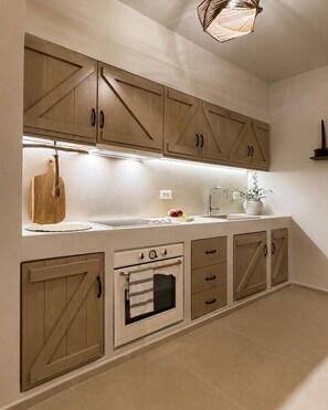 A kitchen with wooden cabinets, a built-in oven, and a hanging wooden cutting board. - Conte Maris II - Sea View Mediterranean Escape (Tragaki)