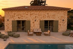 A stone building with a tiled roof, two sliding glass doors, and a pool area with lounge chairs. - Conte Maris II - Sea View Mediterranean Escape (Tragaki)
