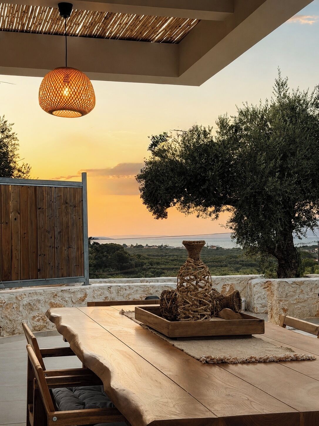 An outdoor seating area with a wooden table, a woven basket, and a hanging light fixture.