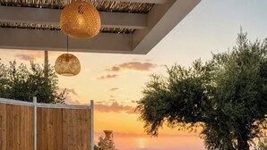 An outdoor dining area with a wooden table and chairs, a woven ceiling, and a view of the sea at sunset. - Conte Maris II - Sea View Mediterranean Escape (Tragaki)
