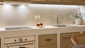 A kitchen with wooden cabinets, a built-in oven, a sink, and a potted plant. - Conte Maris II - Sea View Mediterranean Escape (Tragaki)