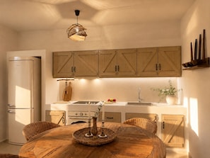 Une cuisine avec des meubles de rangement en bois, une table ronde en bois et un luminaire suspendu.