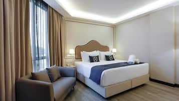 Una habitación de hotel con cama, sofá, mesita de noche y ventana con cortinas.