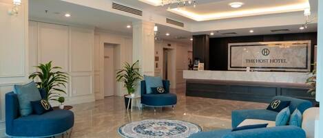 A hotel lobby with a reception desk, blue sofas, a chandelier, and a marble floor.