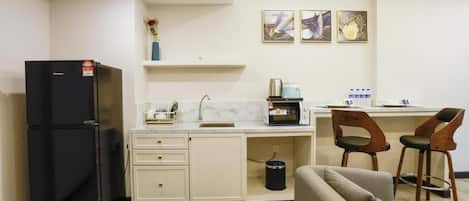 A compact kitchen with a refrigerator, microwave, sink, and bar stools.