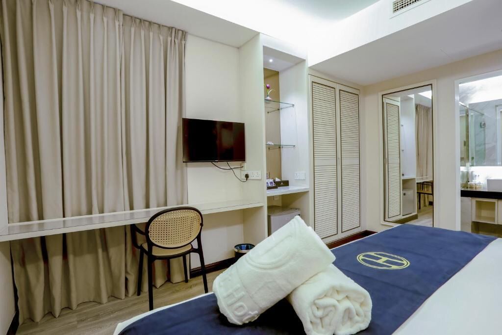 A hotel room with a bed, a television, a chair, a desk, a mirror, and a wardrobe.