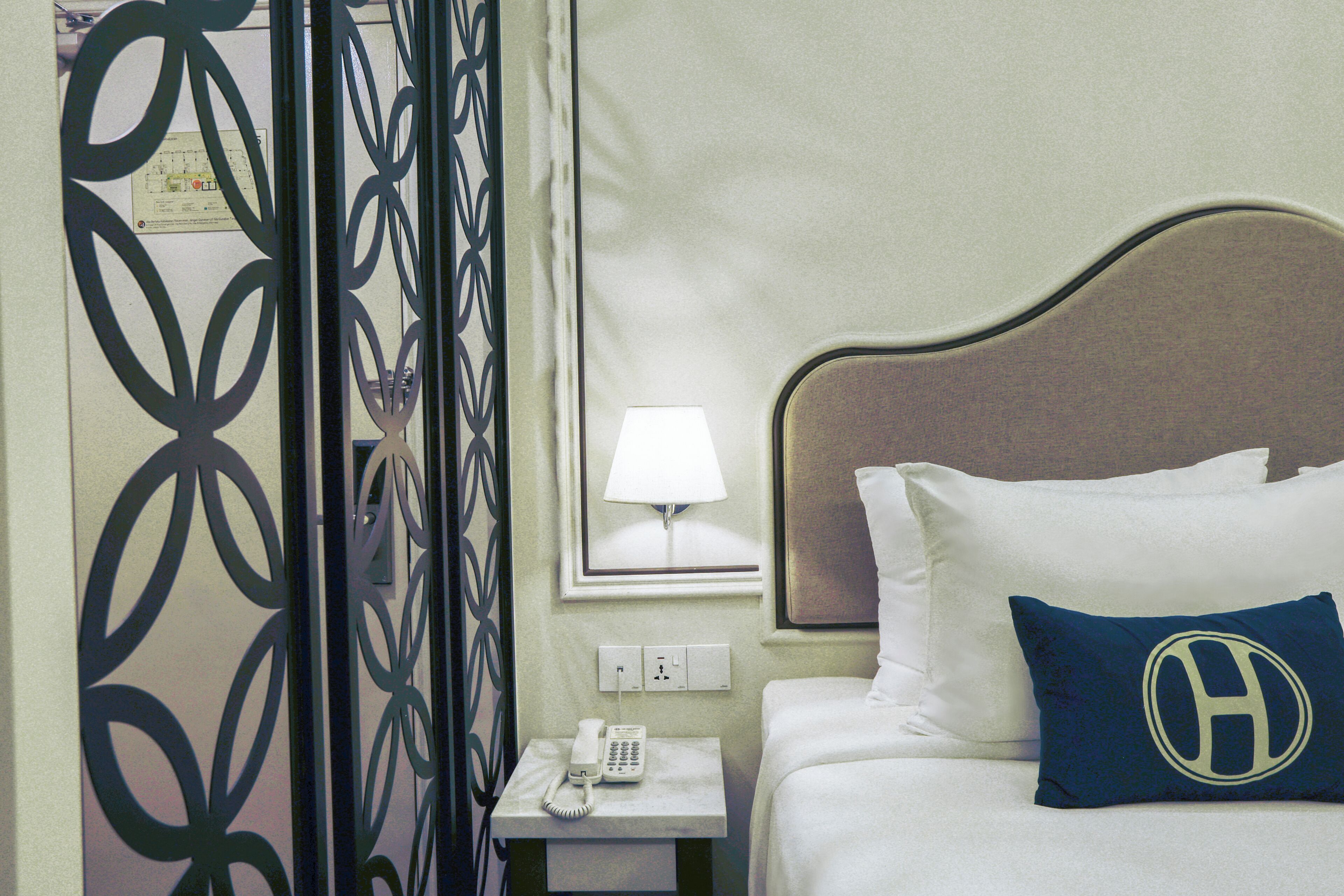 A hotel room with a bed, a nightstand with a lamp, a phone, and a decorative wall panel.