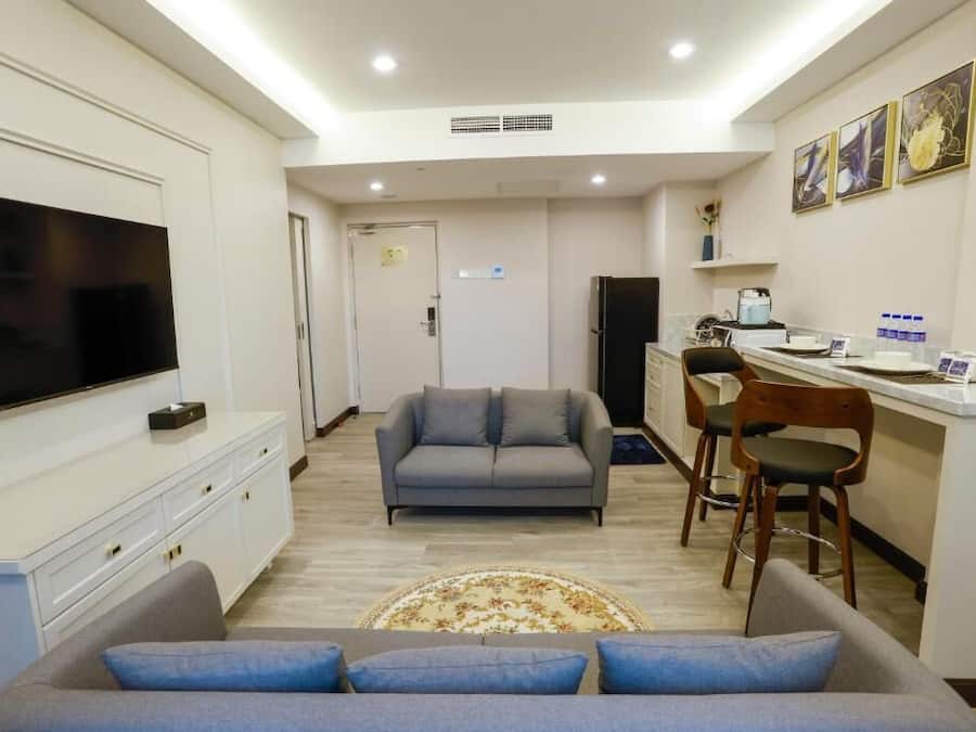 Una sala de estar moderna con un televisor de pantalla plana, un sofá gris y un comedor con taburetes de bar.