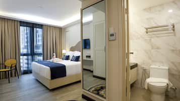 A hotel room with a bed, a chair, a bathroom with a toilet and shower, and a mirror.