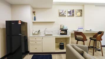 A compact kitchen with a refrigerator, microwave, sink, and two bar stools.