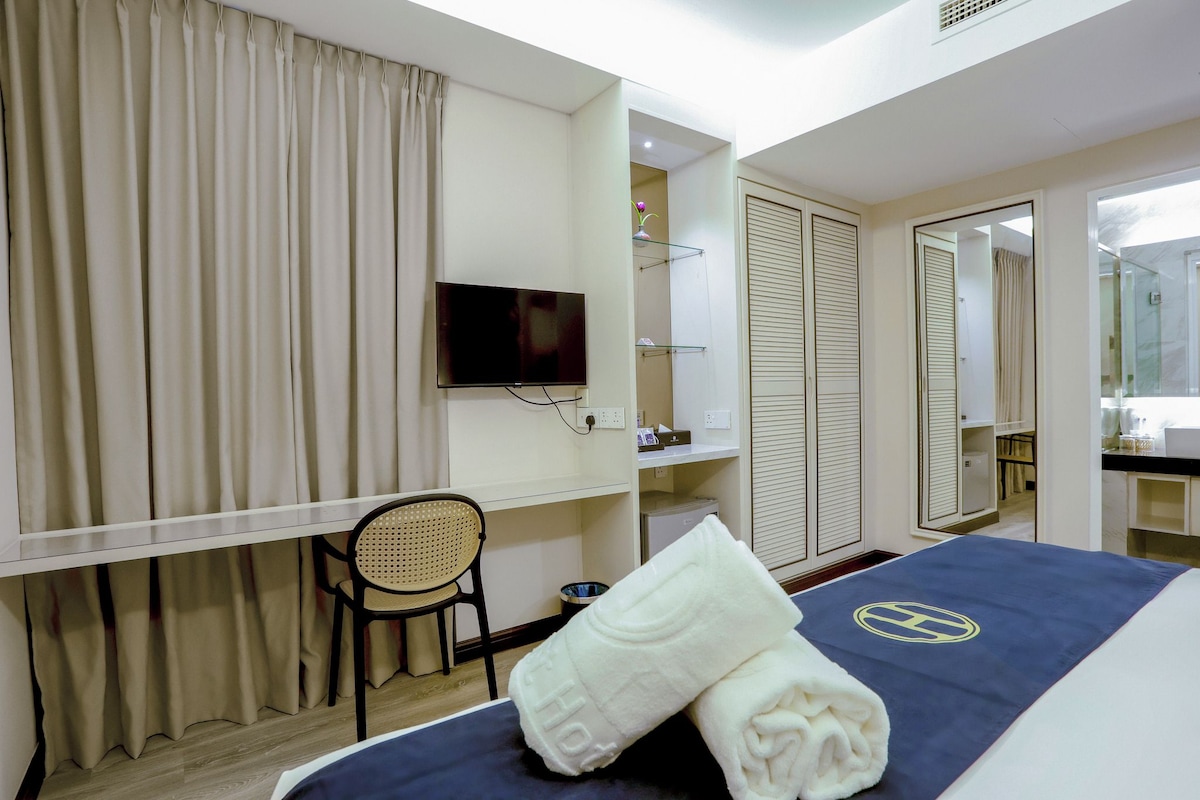 A hotel room with a bed, a television, a chair, a desk, and a wardrobe.