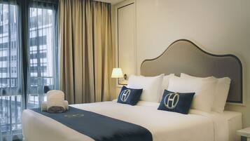A hotel room with a bed, a nightstand, a lamp, and a window with curtains.