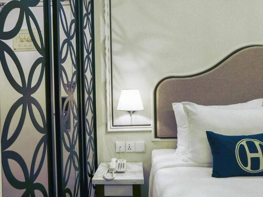 Quarto de hotel com cama, mesa de cabeceira com telefone, abajur e painel decorativo na parede.