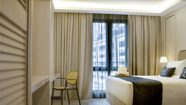 A hotel room with a bed, a chair, a nightstand, a lamp, and a window with curtains. - THE HOST HOTEL (Ipoh)