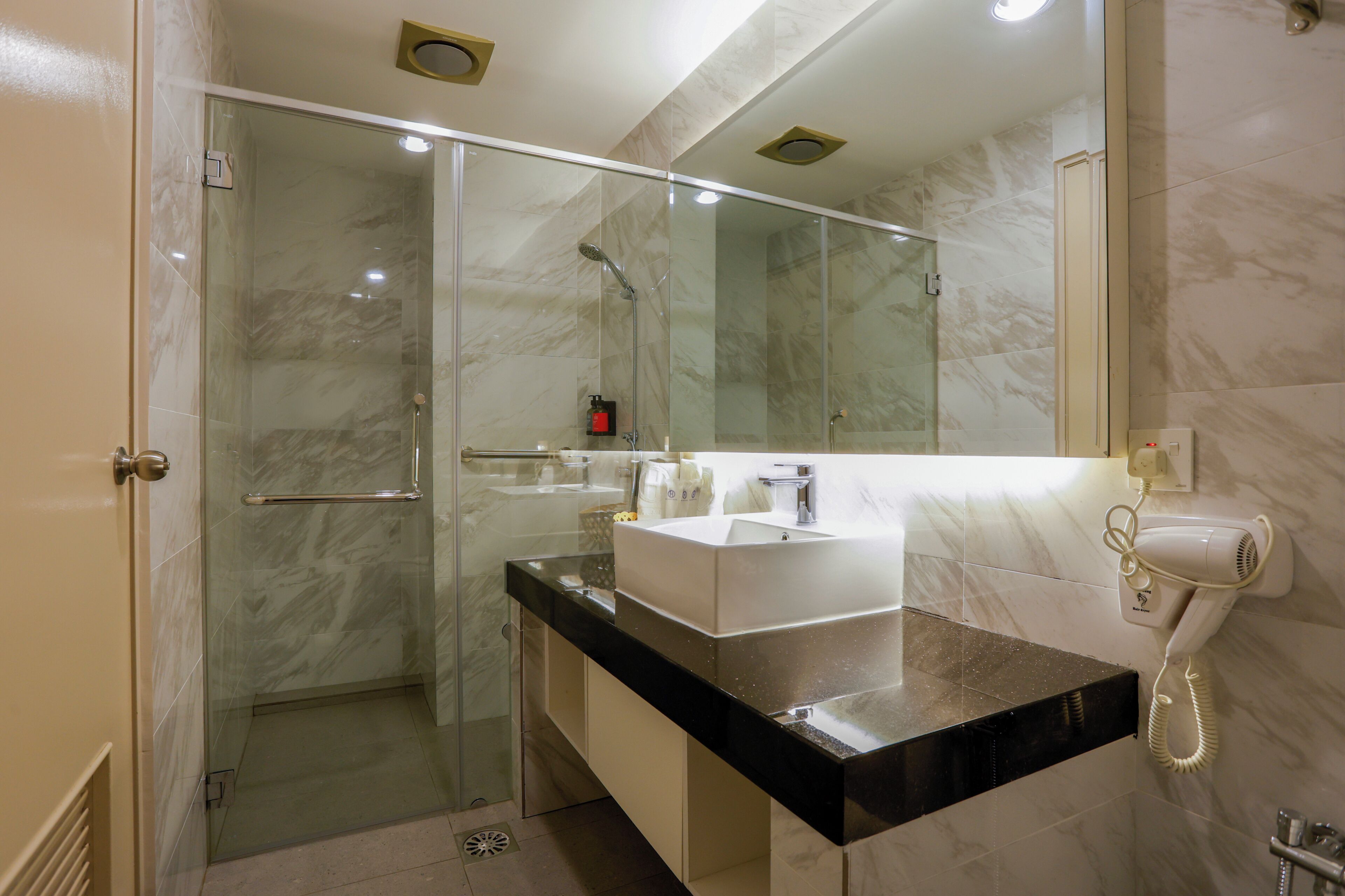 Une salle de bain moderne avec une douche à parois de verre, un lavabo blanc et un sèche-cheveux posé sur le comptoir.