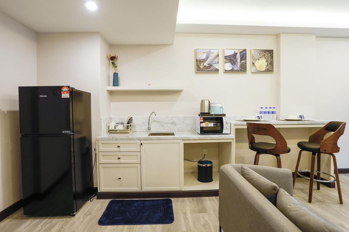 A compact kitchen with a refrigerator, microwave, sink, and two bar stools.