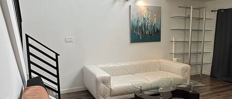 En moderne stue med en sort sofa, en hvid sofa, et sofabord i glas, et maleri på væggen og trægulv.