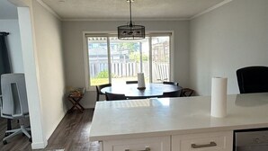 A kitchen with a central island, a dining area with chairs, a large window, and a ceiling fan.