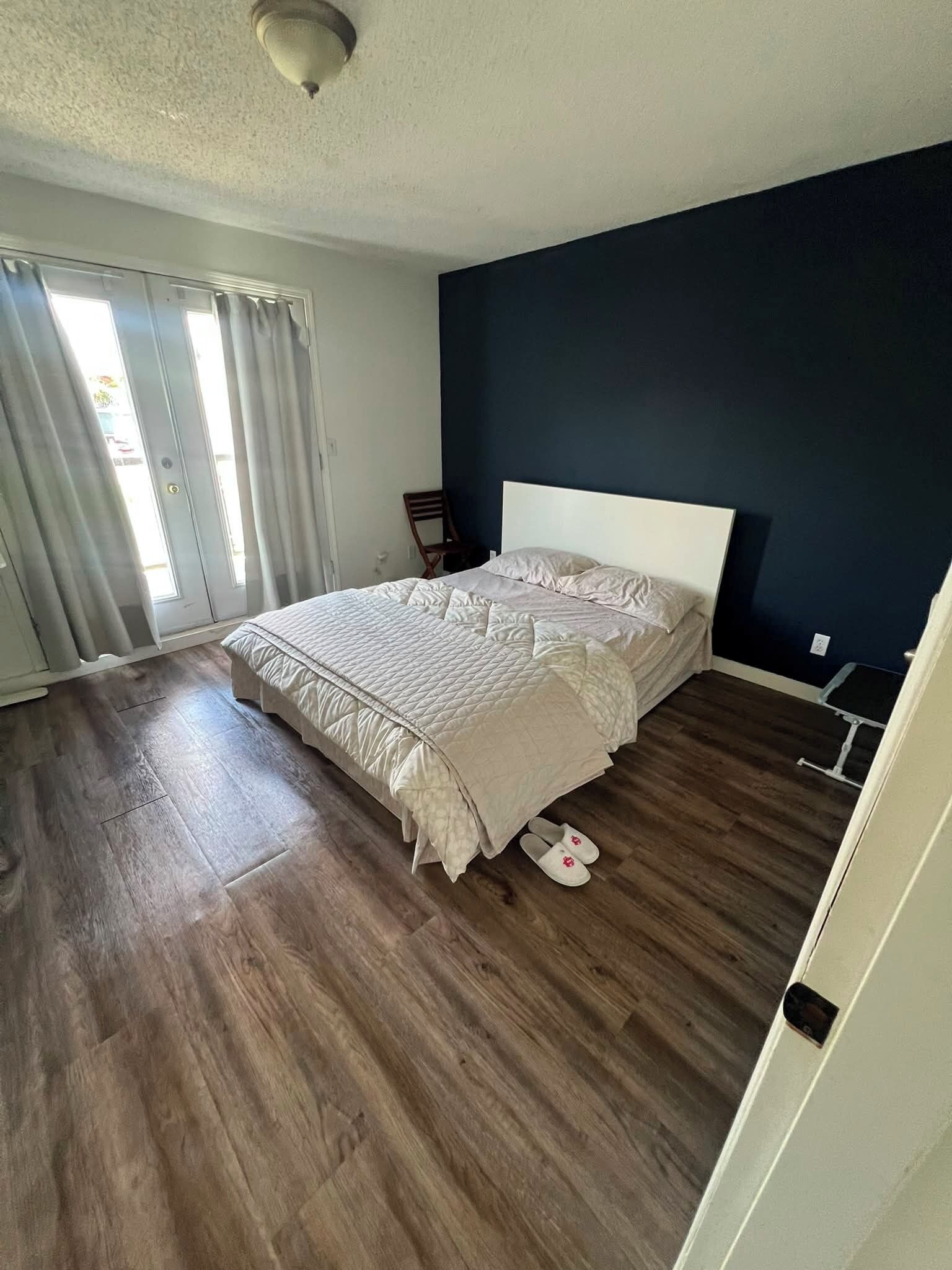 Une chambre à coucher avec un lit, un plancher en bois, une fenêtre avec des rideaux et un luminaire au plafond.