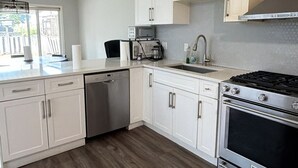 A modern kitchen with white cabinets, a dishwasher, a stove, and a sink.