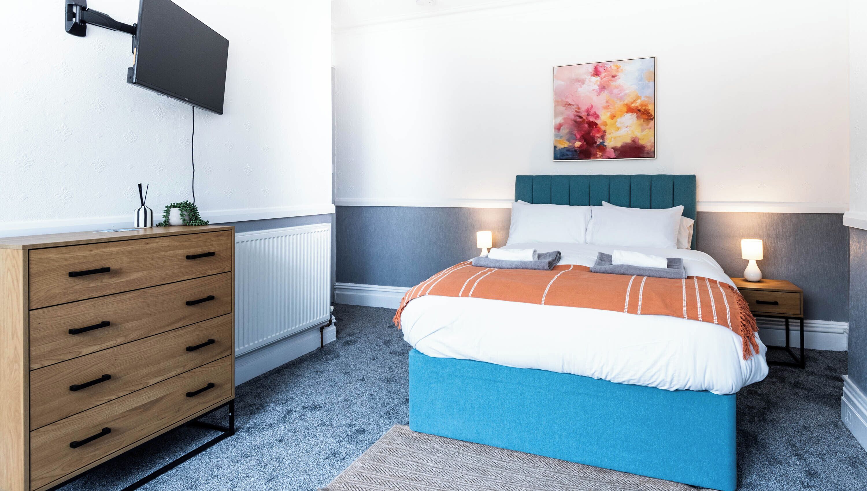 A modern bedroom with a bed, bedside tables, a dresser, a radiator, and a wall-mounted TV.