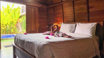 A wooden room with a bed, a view of greenery outside, and a door.