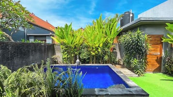A swimming pool with surrounding greenery and a house with a red roof.