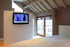 Ein Schlafzimmer mit Fernseher an der Wand, einem Bett und einer Glastür zum Außenbereich.