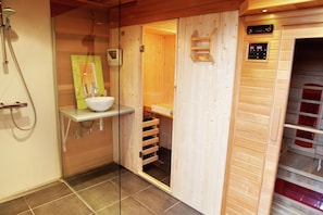 Ein Saunaraum aus Holz mit Glastür, Waschbecken und Bedienfeld.