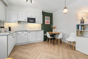 A modern kitchen with white cabinets, a herringbone floor, a dining table with chairs, and a bookshelf. - 1 bedroom accommodation in Nieuwpoort (Nieuwpoort)