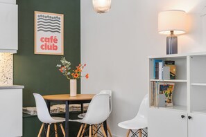 A modern dining area with a table, chairs, a vase of flowers, a wall-mounted lamp, and a bookshelf with books. - 1 bedroom accommodation in Nieuwpoort (Nieuwpoort)