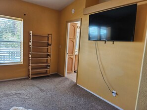 A room with a TV mounted on the wall, a window with blinds, and a carpeted floor. - The Spring Meadow House. (Willits)
