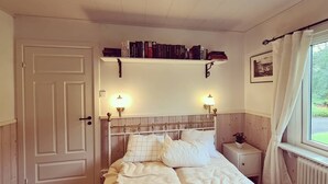 Um quarto com cama, abajures, estante de livros, janela com cortinas e porta.