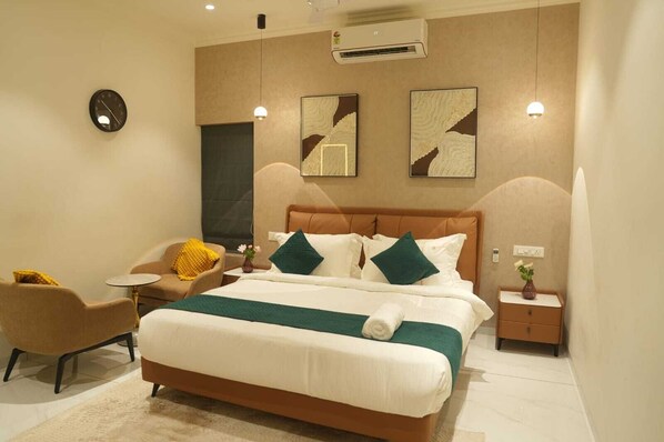 Una habitación de hotel moderna con una cama grande, una silla, una mesita y una mesita de noche.