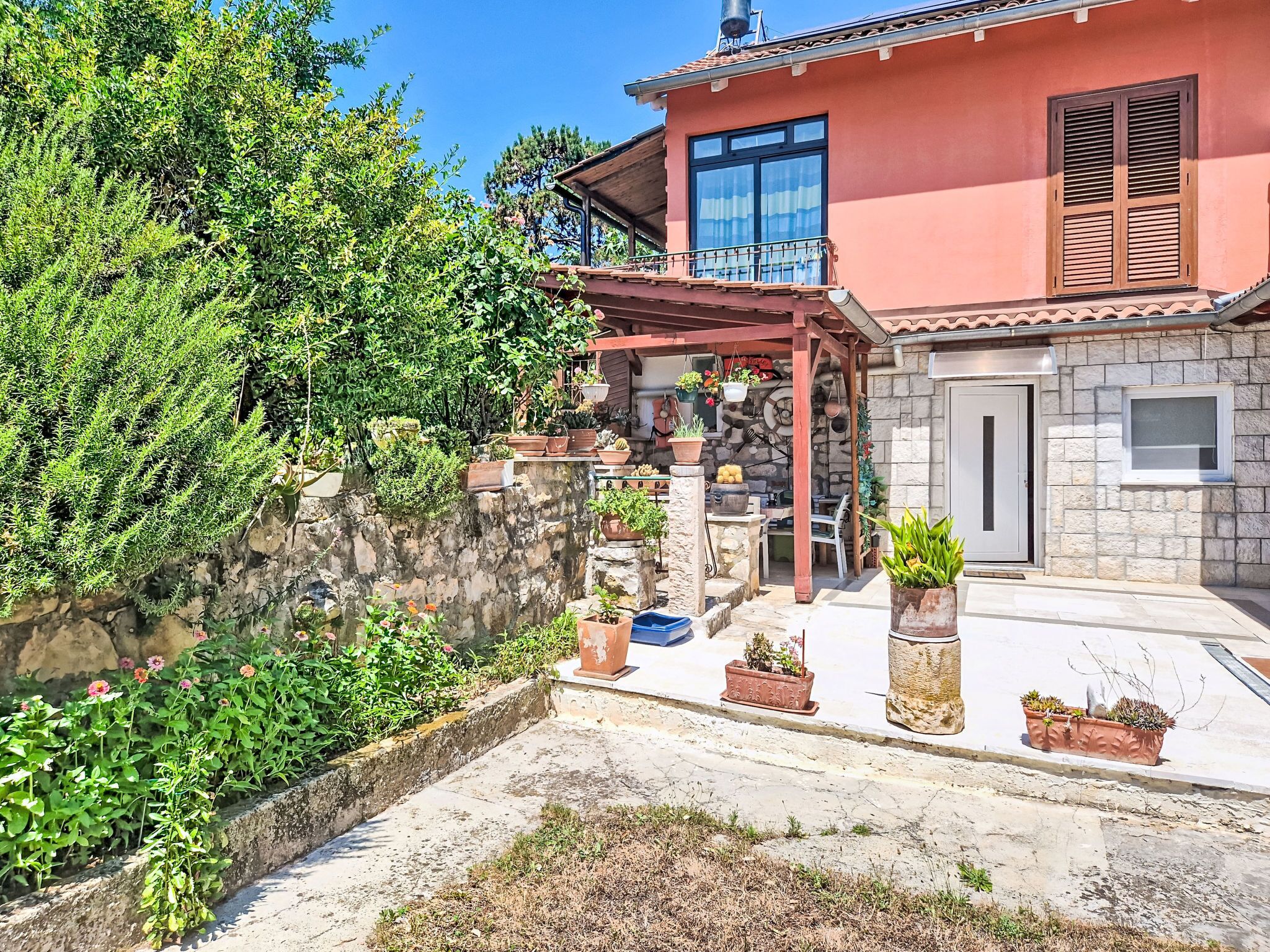 A house with a stone facade, a balcony with potted plants, and a clear sky.