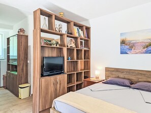 A bedroom with a bed, a wooden TV stand, a nightstand, and a wall painting. - Apartment Monte by Interhome (Umag)