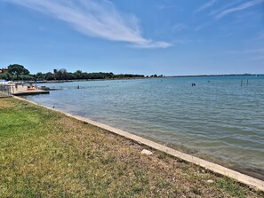 A waterfront area with a grassy embankment and a pier extending into calm water. - Apartment Monte by Interhome (Umag)