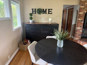 Ein Essbereich mit rundem Tisch, Stühlen, einer dekorativen Vase, einem Kamin und einem an der Wand befestigten Schild mit der Aufschrift 'HOME'.
