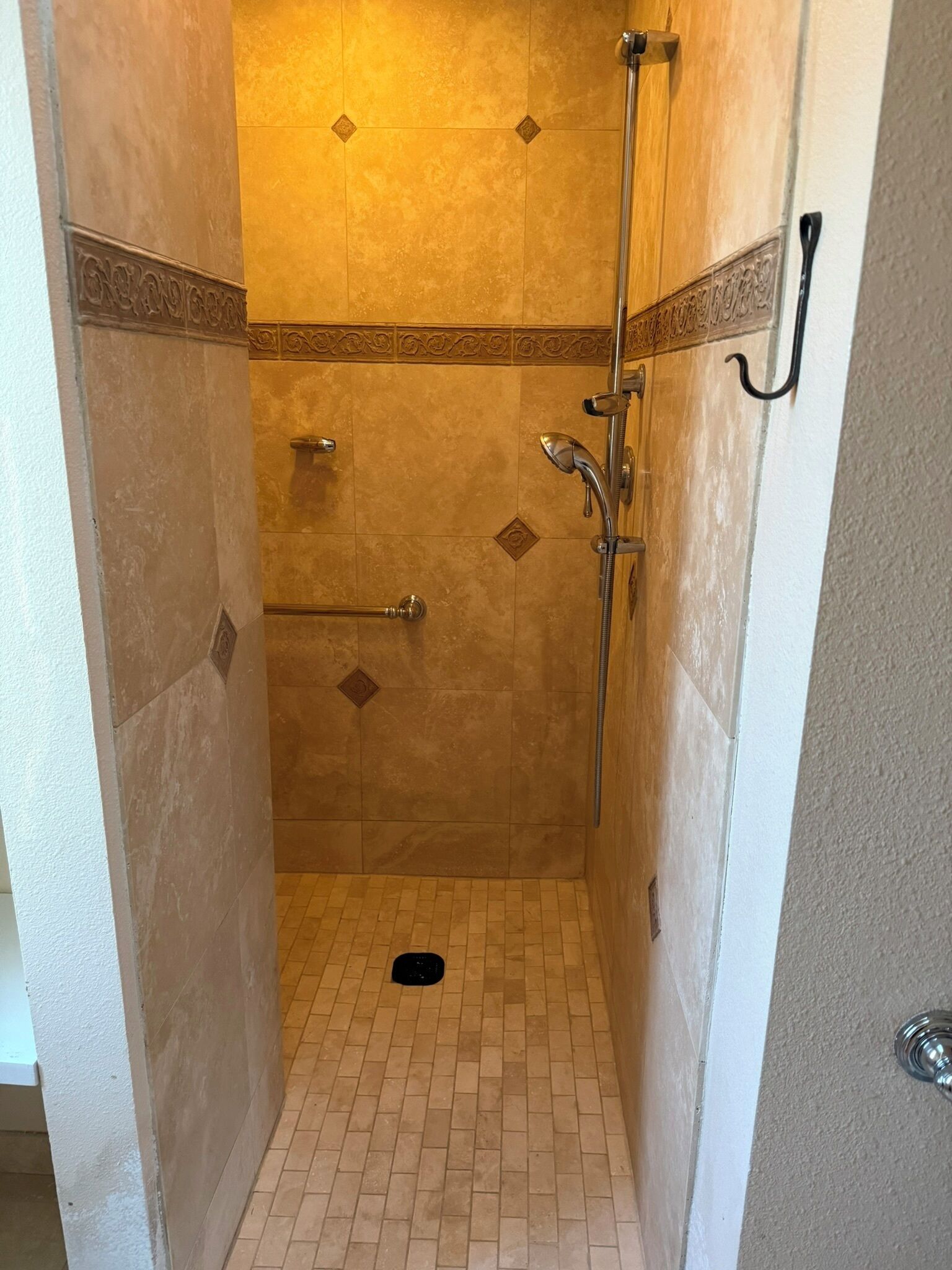 A small, enclosed shower area with tiled walls and floor, a handheld showerhead, and a handheld shower head on a stand.