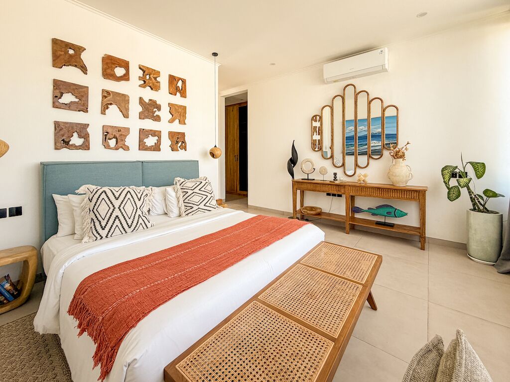 A bedroom with a bed, a bedside table, a mirror, wall art, and a potted plant.