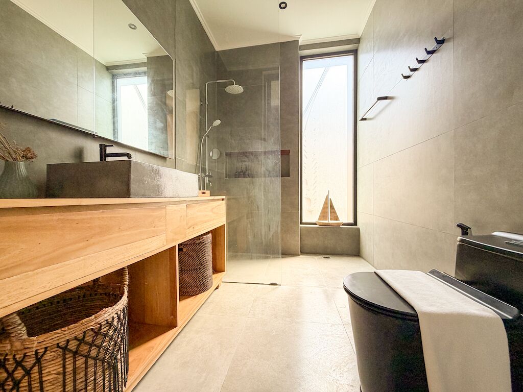 Un baño moderno con tocador de madera, cabina de ducha de vidrio y un espejo grande.