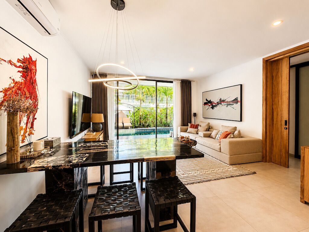 A modern kitchen with a large island, a dining area with benches, a sofa, and a pool view.