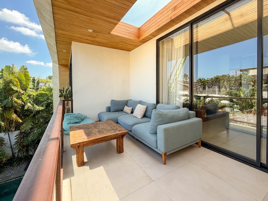 Una sala de estar moderna con un sofá, una mesa de centro y un ventanal de vidrio que da a un balcón con plantas.