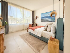 Quarto com cama, escrivaninha, cadeira, janela com cortinas, um quadro e luminária pendente.