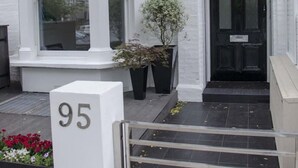 Un edificio bianco con una porta nera, una targa con il numero '95' e un piccolo giardino con fiori rossi.