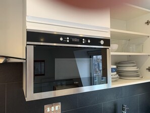 A modern kitchen with a built-in oven, a window, and a counter with stacked dishes. - Zen Studio w/ Spa Shower & AC (Greater London)