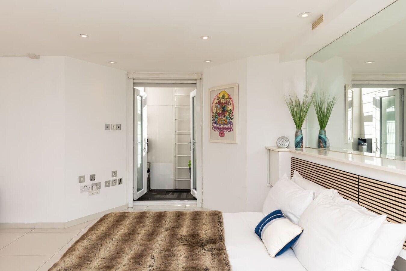 A modern bedroom with a bed, a fluffy rug, a mirror, and a door leading to a bathroom.