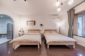 Habitación de hotel con dos camas de madera, una mesita, un refrigerador, un cuadro en la pared y una ventana con cortinas.