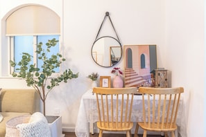 Un comedor con una mesa, sillas, un jarrón con flores, un cuadro enmarcado y un espejo en la pared.