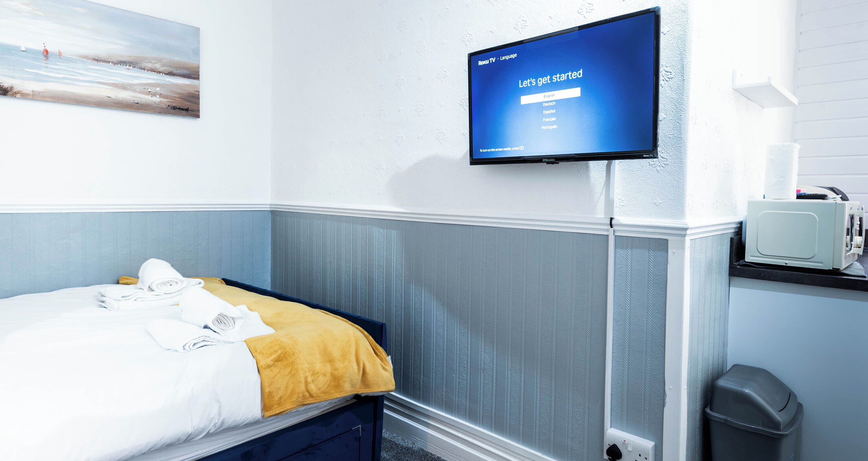 Ett hotellrum med en säng, en tv-skärm som visar ett menyalternativ för språkval, en tavla på väggen och en liten papperskorg.